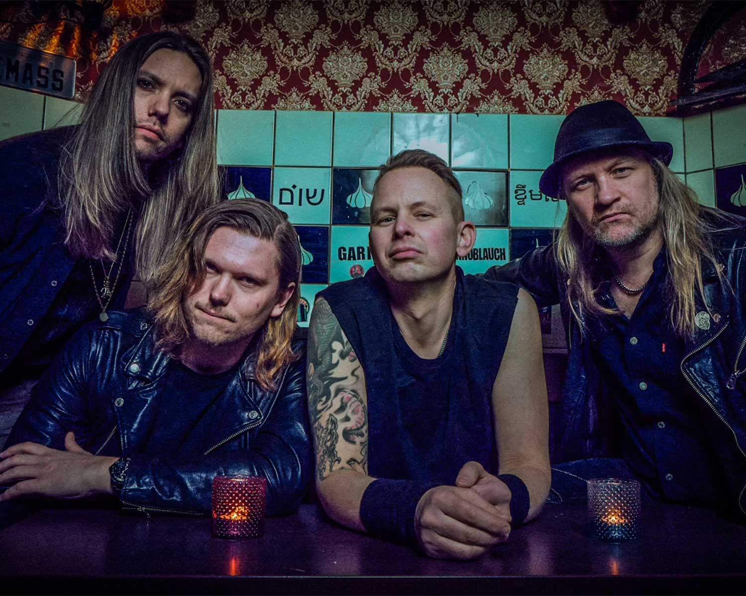 Pressfoto av bandmedlemmarna i Eclipse. De står tillsammans med en bakgrund av kakelplattor med stickers och mönstrad tapet.