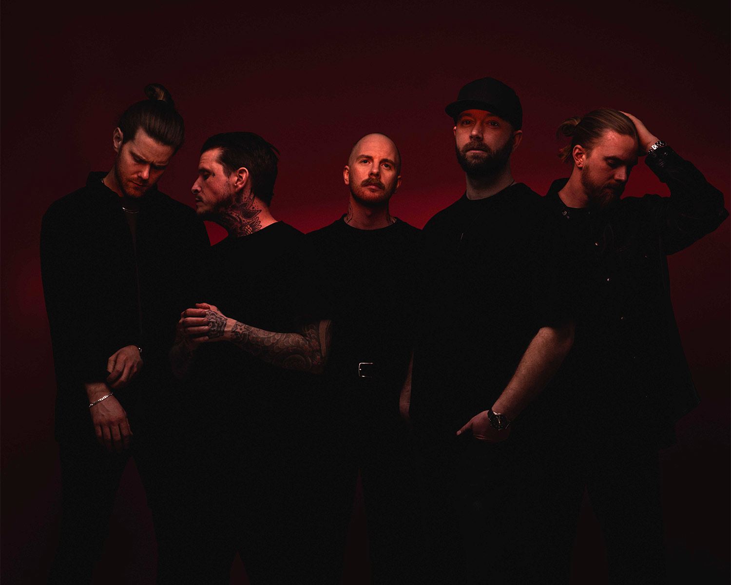 Fem medlemmar i Adept står mot röd bakgrund, klädda i svarta kläder med allvarliga uttryck.