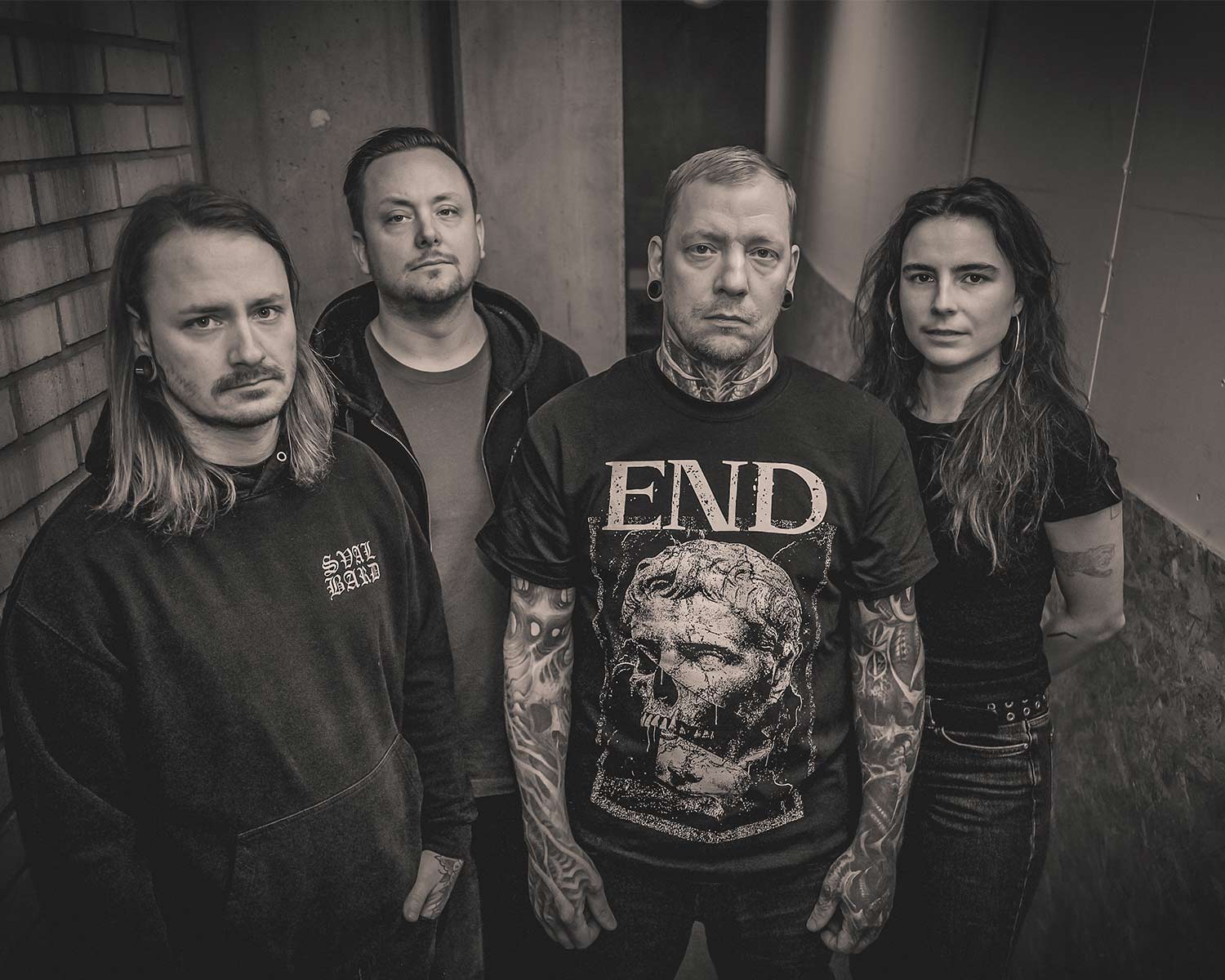 Fyra bandmedlemmar i bandet KLPS poserar tätt tillsammans i en mörk miljö med dramatisk belysning.