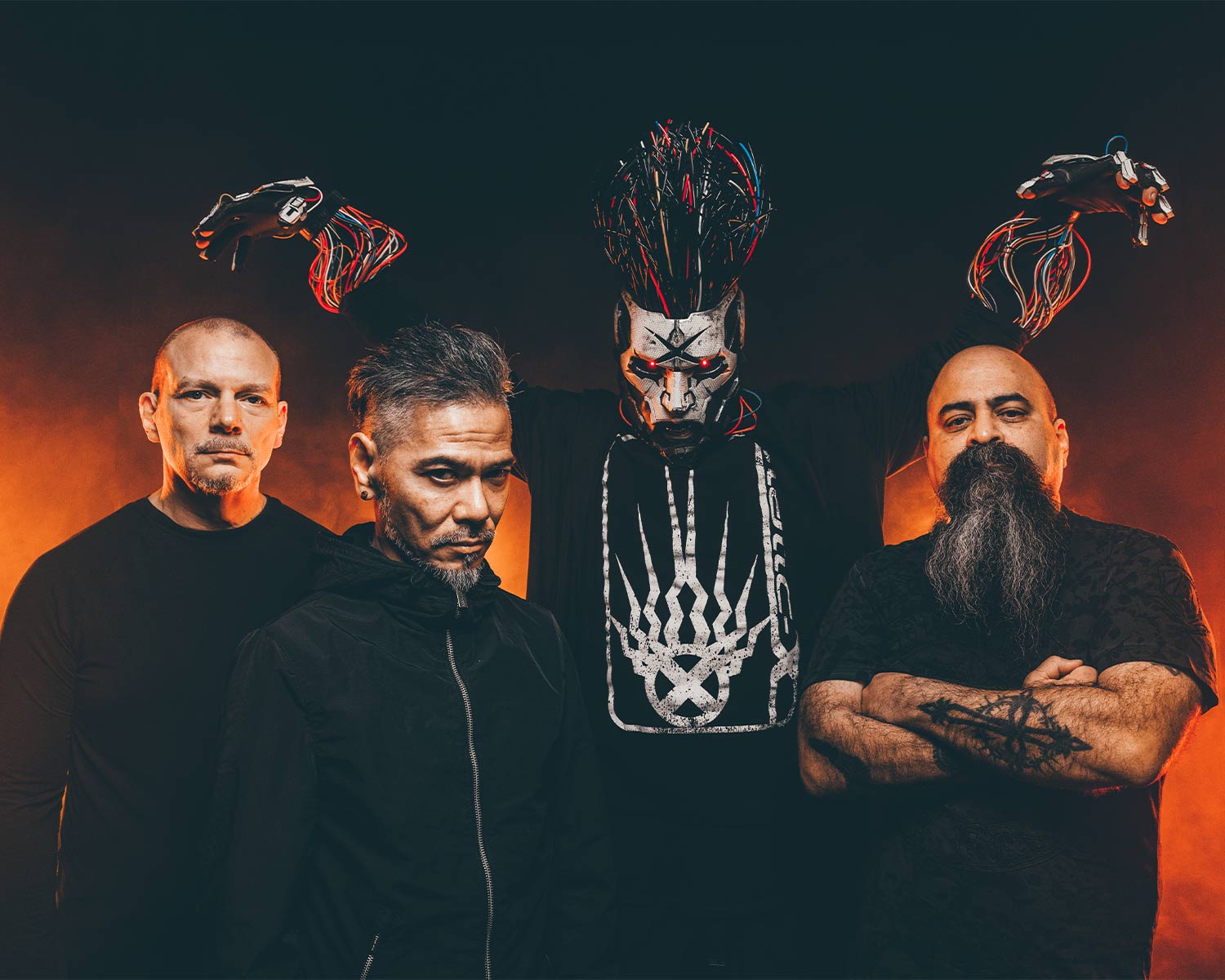 Pressbild av Static-X: fyra bandmedlemmar står mot mörk bakgrund med orange ljus. Tre medlemmar bär svarta kläder, och den fjärde bär en mask med lysande röda ögon och håller upp kablar i händerna.