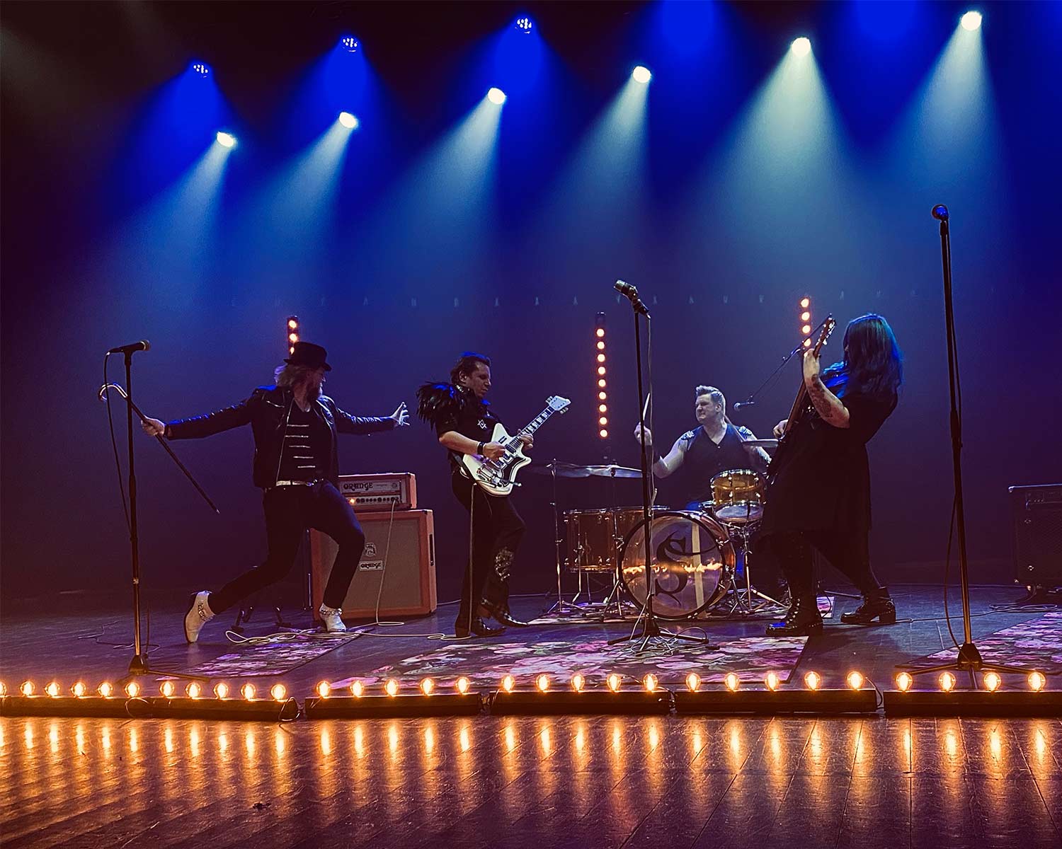 The Striders spelar live på scen med gitarrer och trummor under färgstark ljussättning.