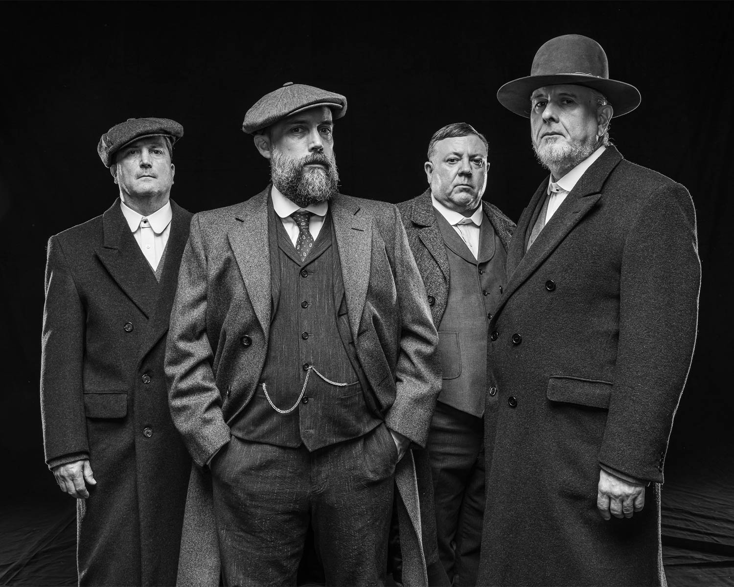 The members of Clutch pose in suits and hats against a dark background in black and white.