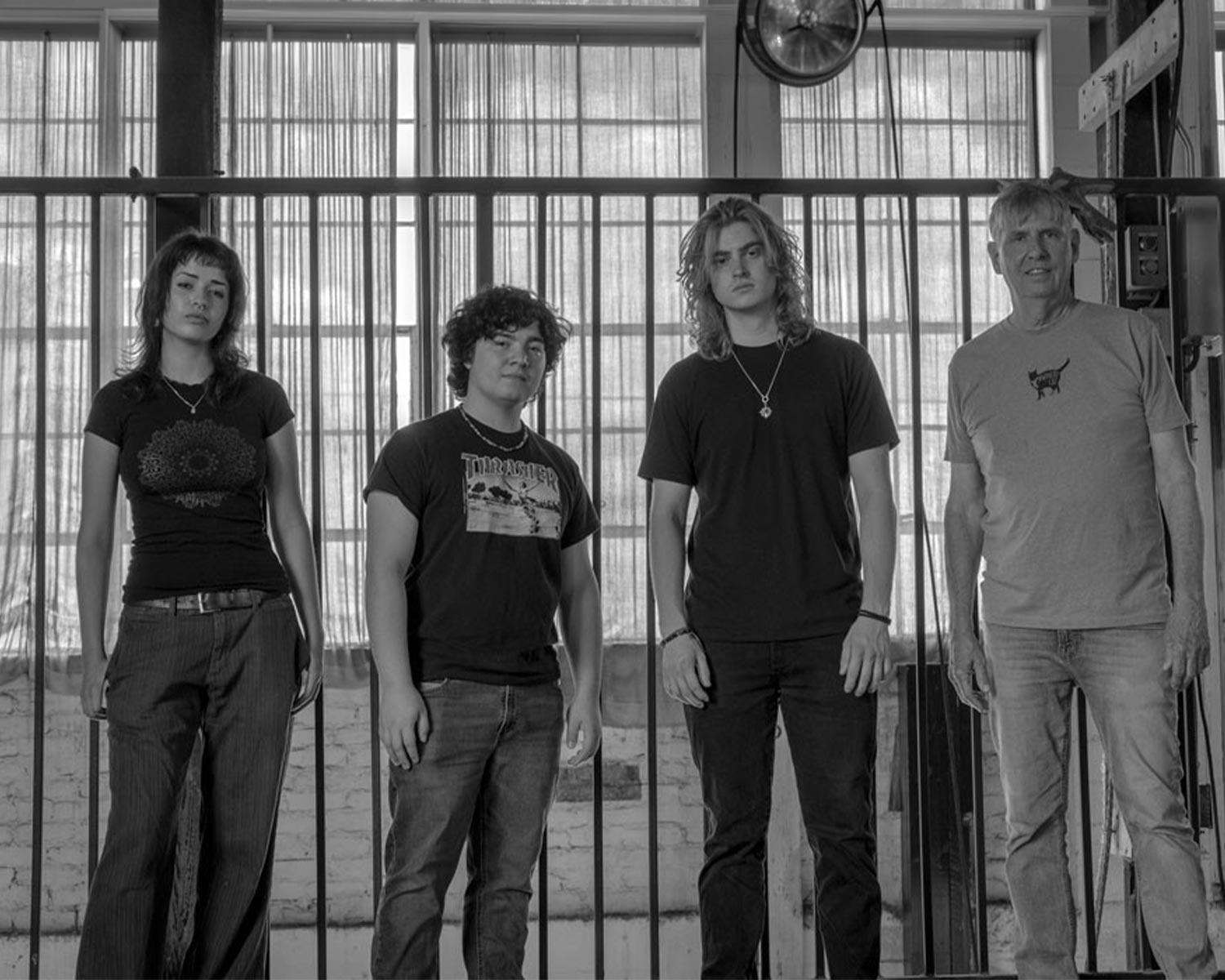 The members of Black Flag pose in front of a fence in black and white.