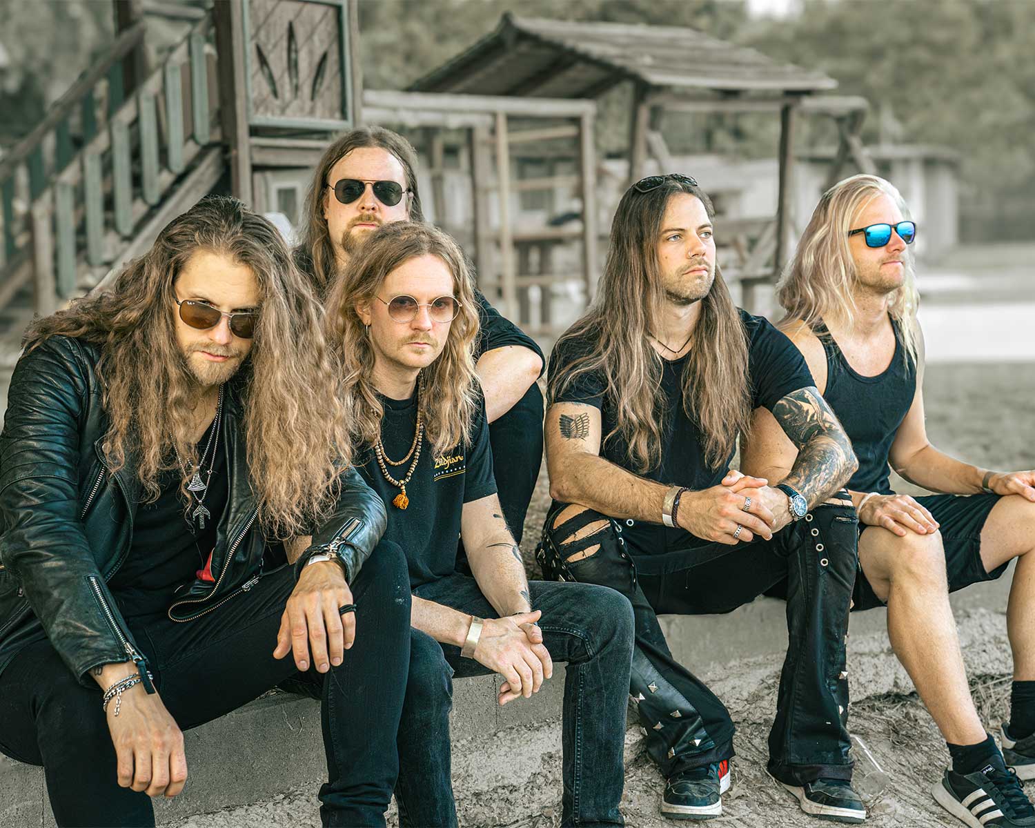 The members of Dynazty are sitting together outdoors in front of a wooden building.