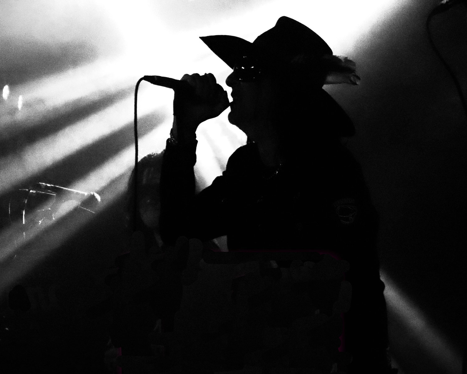 The singer from Faster Pussycat is singing into a microphone on stage in black and white.