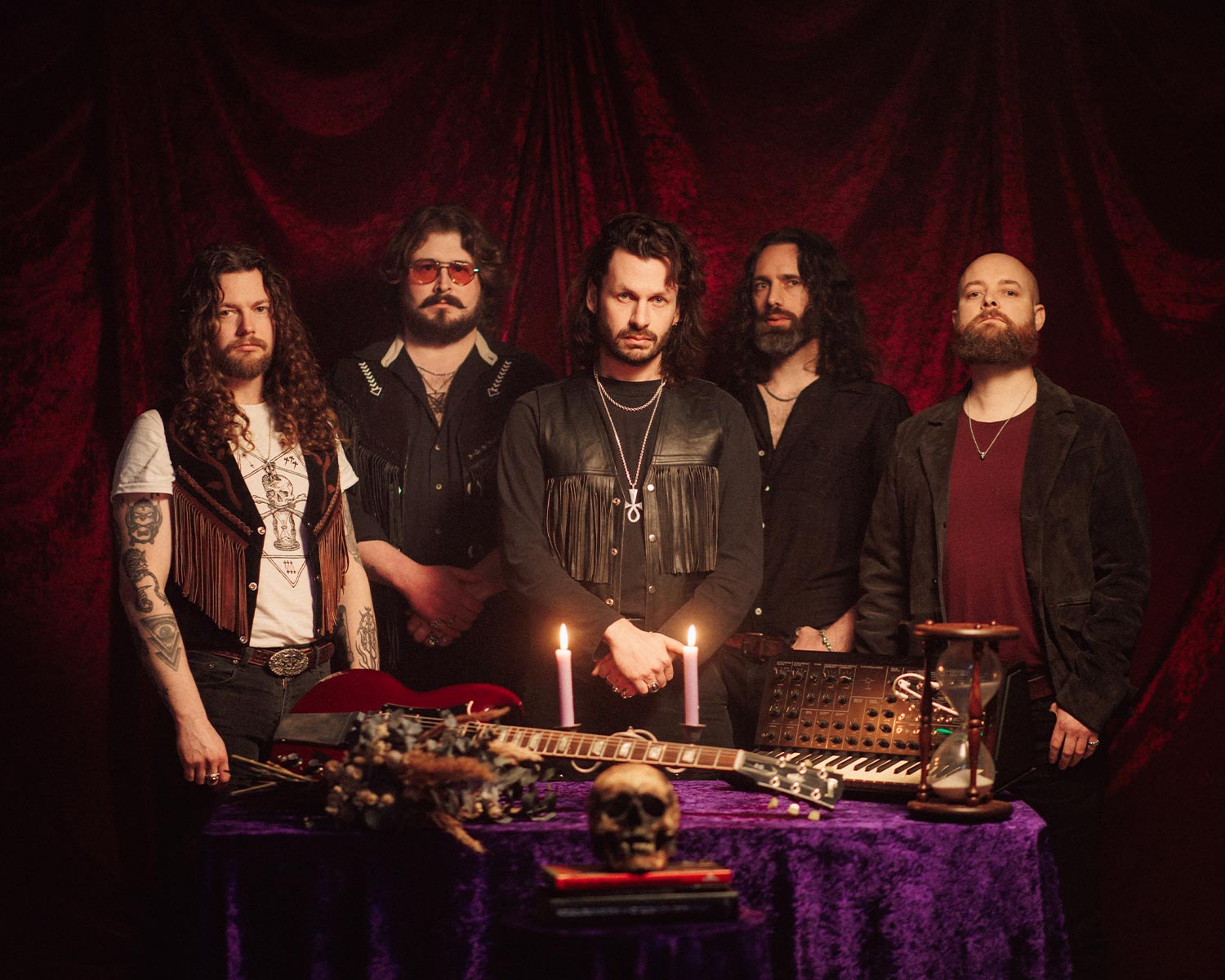 The members of Green Lung pose behind a table with candles, instruments, and a skull.