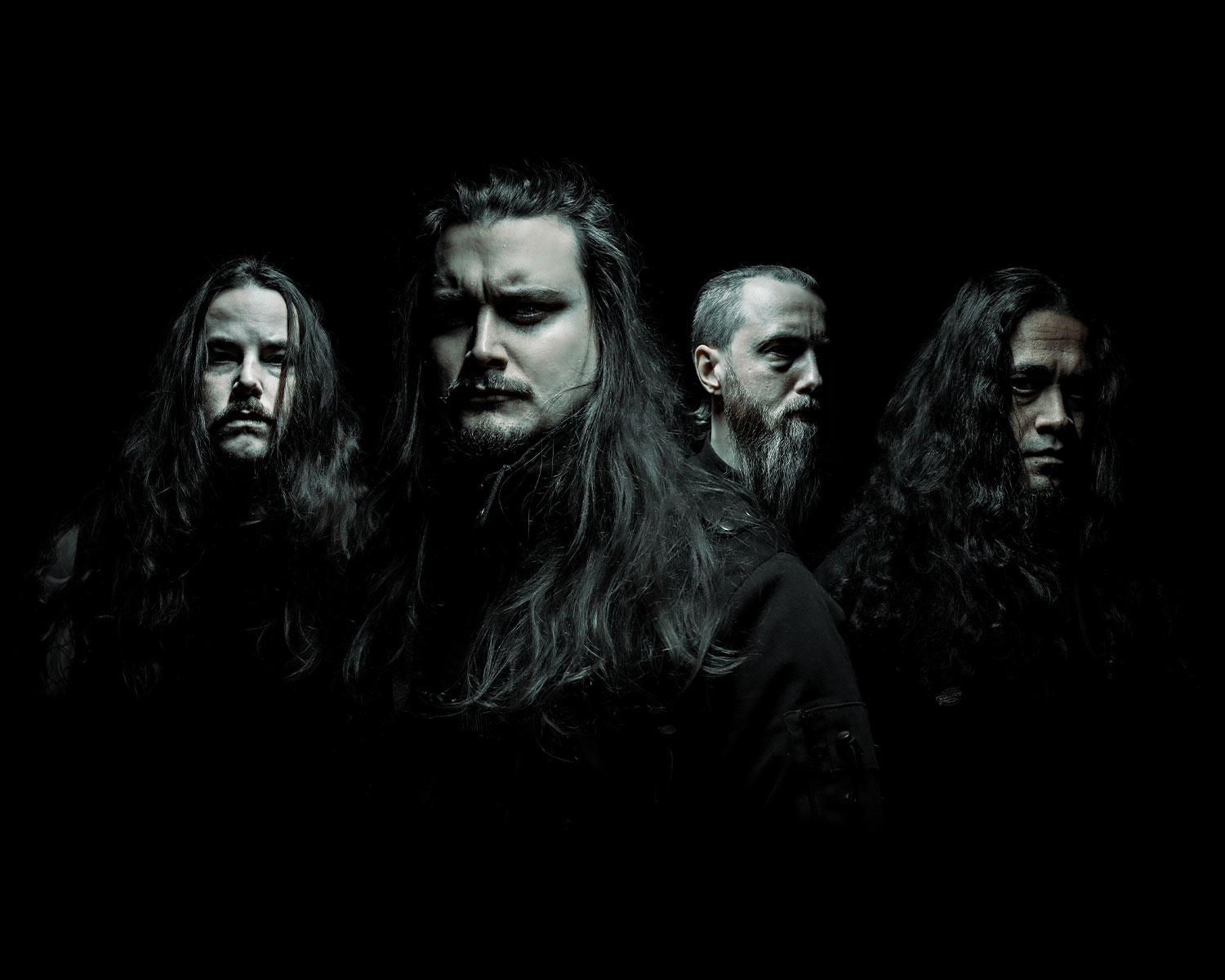 Four members of the band are posing in a dark setting.