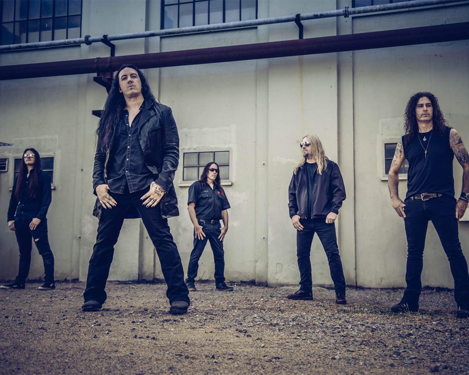 The members of Sanctuary pose together in front of a bright industrial building.