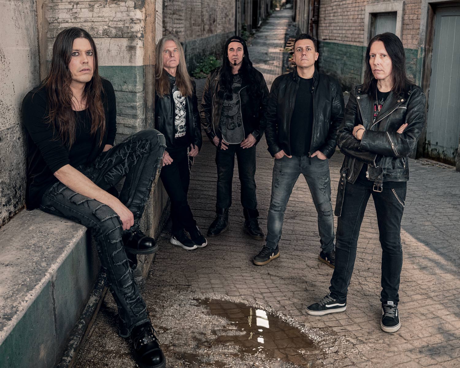 The members of Shakra pose in a narrow alley with weathered brick walls.